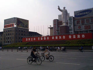 la statue de mao et autour de lui, les panneaux publicitaires